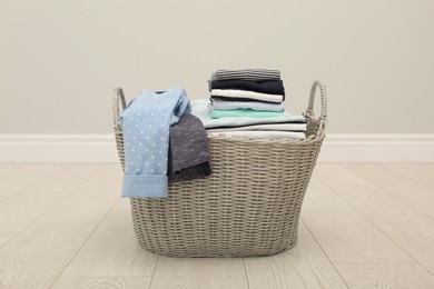 Photo of Wicker basket with folded clothes on floor in room