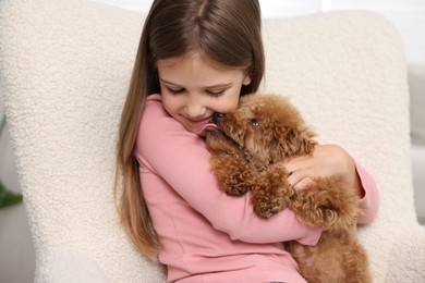 Photo of Little child with cute puppy in armchair indoors. Lovely pet