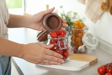Photo of Woman pickling glass jar of tomatoes at counter in kitchen, closeup