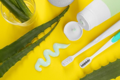 Photo of Aloe vera toothpaste, brushes and green leaves on yellow background, flat lay