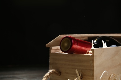 Photo of Wooden crate with bottle of wine on dark background, closeup. Space for text