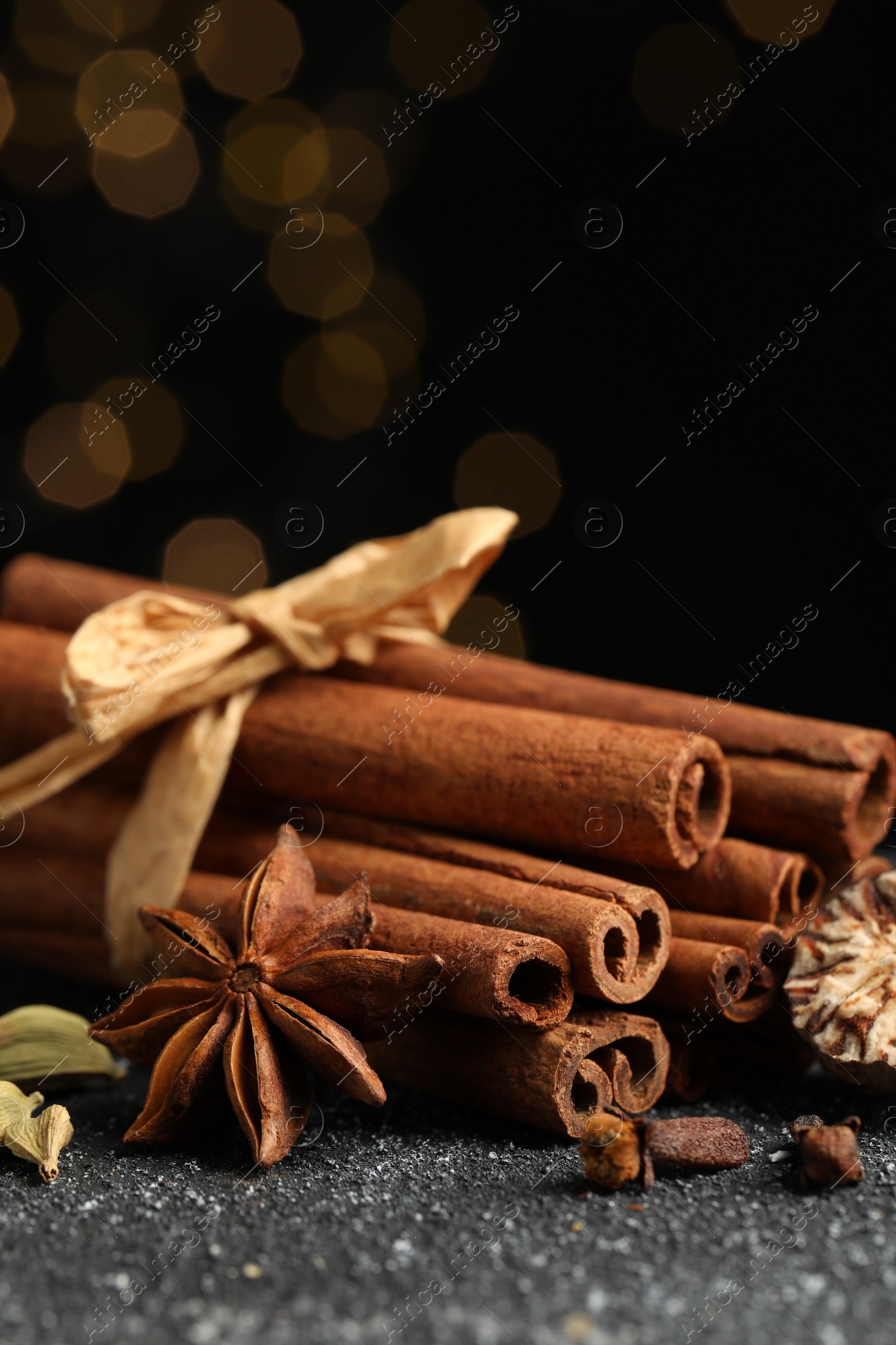 Photo of Different aromatic spices on grey textured table against black background, closeup