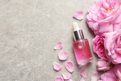 Photo of Bottle of rose essential oil, petals and flowers on grey table, flat lay. Space for text