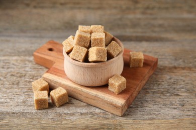 Photo of Brown sugar cubes in bowl on wooden table, closeup