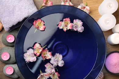 Bowl of water with flowers and different spa supplies on table, top view