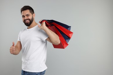 Photo of Happy man with many paper shopping bags showing thumb up on grey background. Space for text