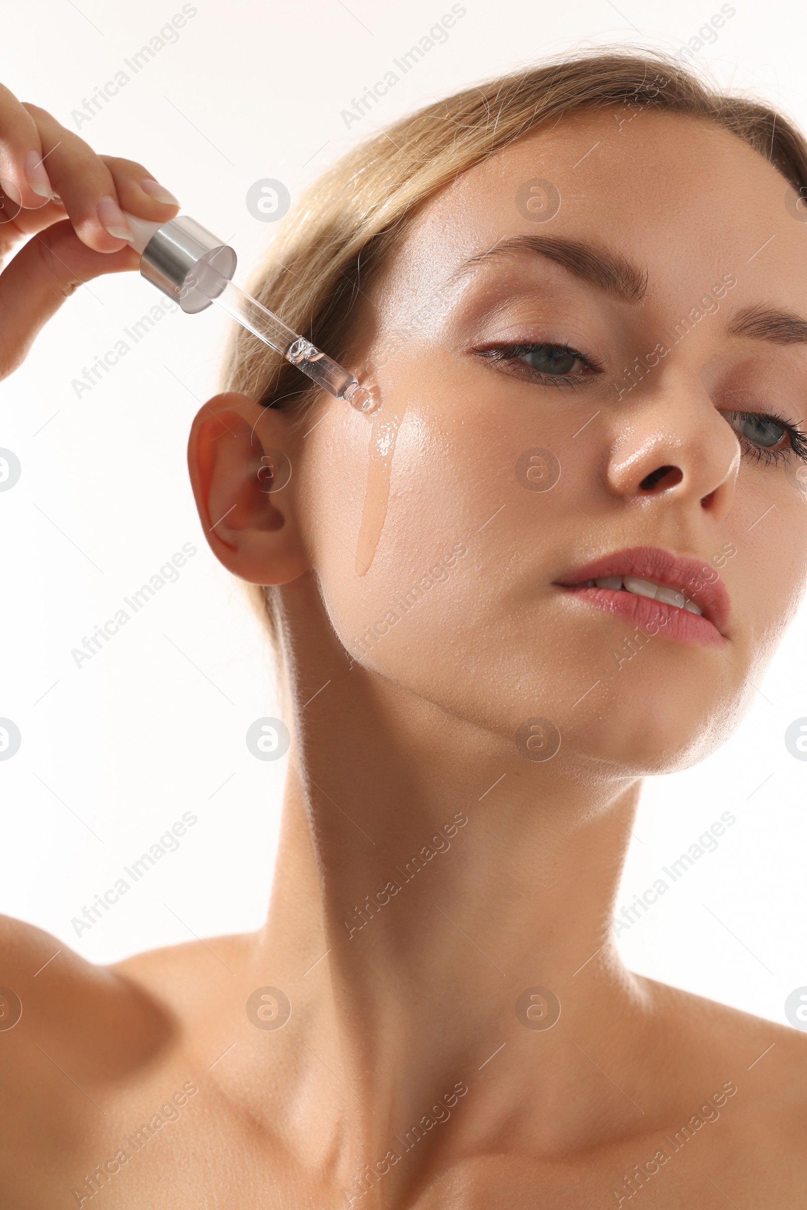 Photo of Beautiful woman applying cosmetic serum onto her face on white background