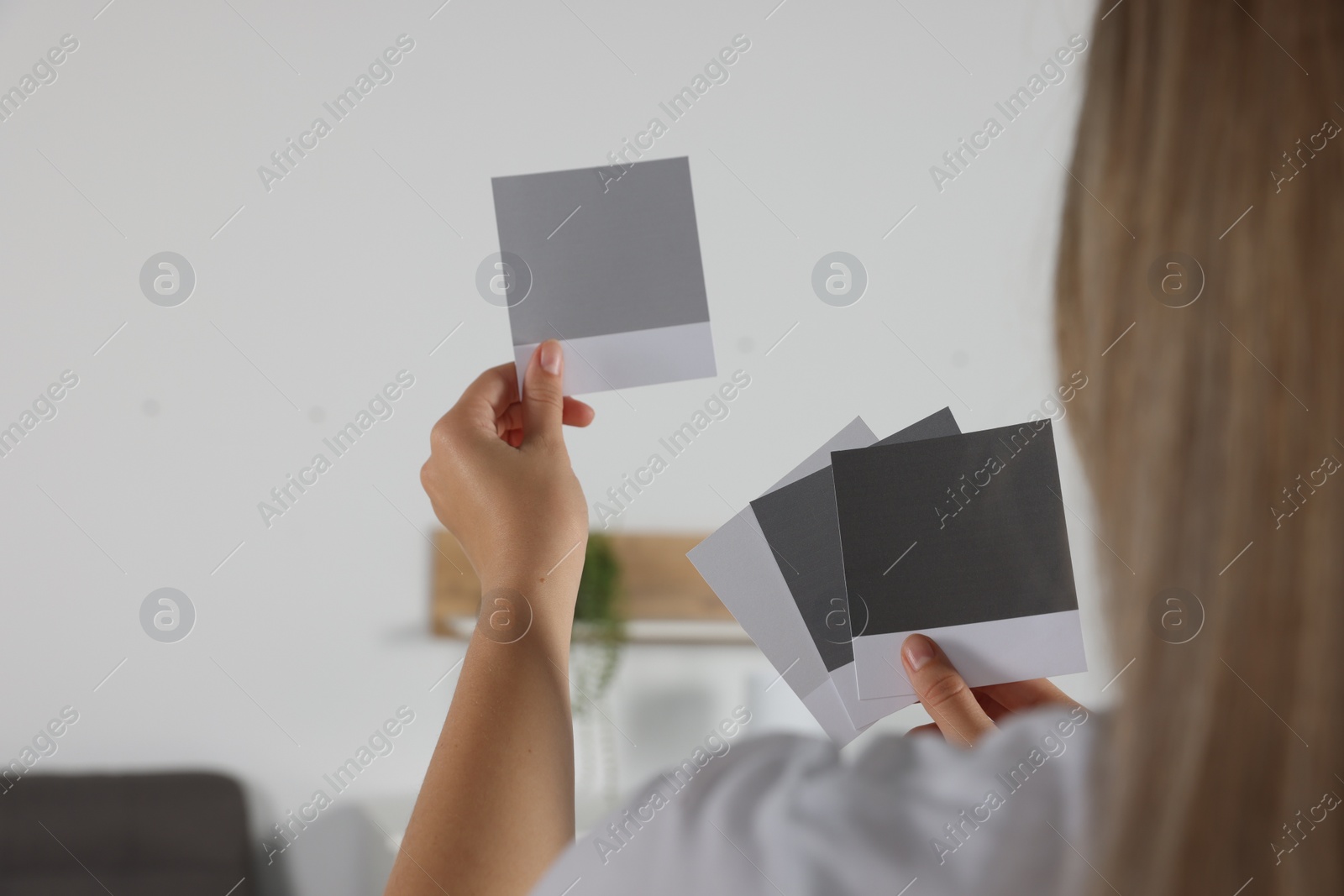 Photo of Woman choosing paint shade for wall in room, focus on hands with color sample cards. Interior design