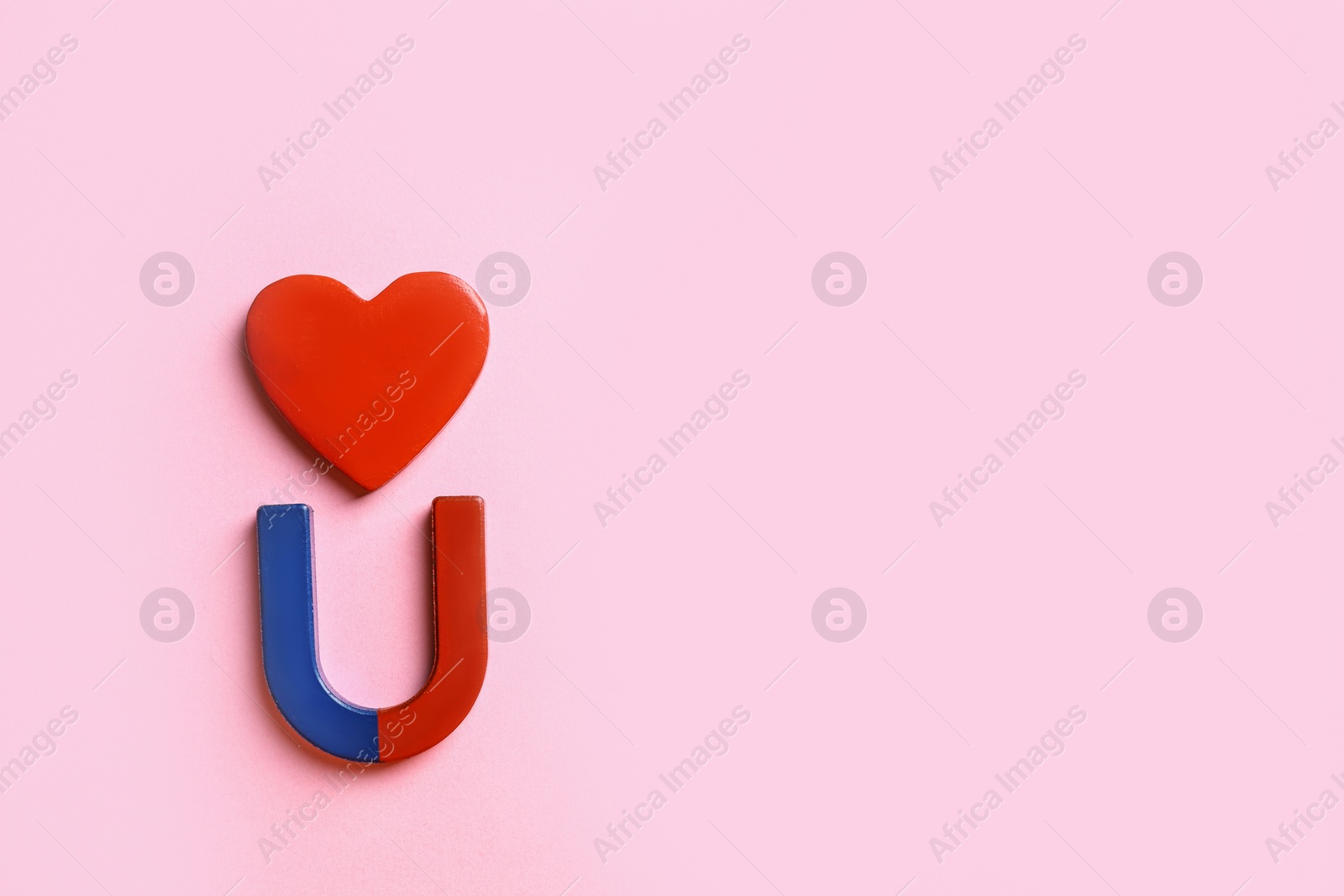 Photo of Red and blue horseshoe magnet with heart on pink background, flat lay. Space for text