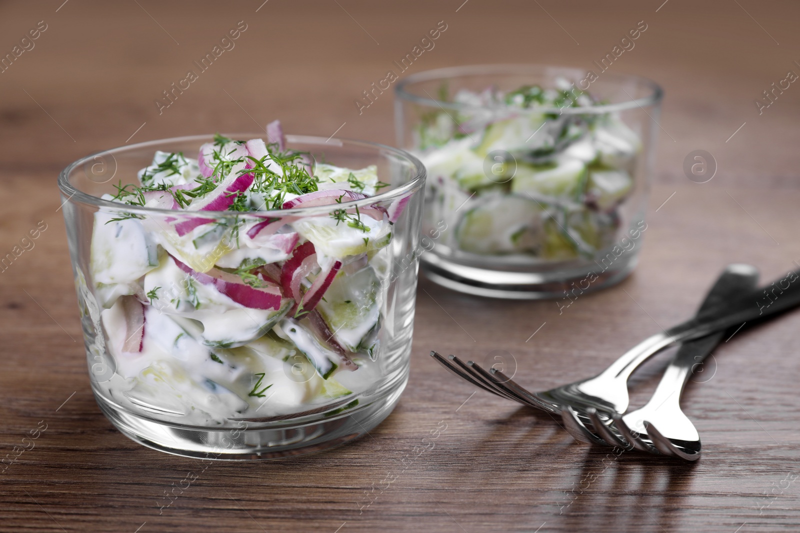 Photo of Glass bowls of vegetarian salad with cucumber and onion on table, closeup