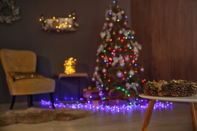 Photo of Beautiful wreath with pine cones on table and Christmas tree in dark room