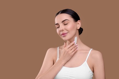 Photo of Beautiful woman with smear of body cream on her neck against light brown background, space for text