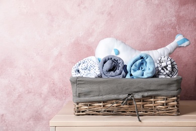Photo of Basket with baby clothes on table near color wall. Space for text