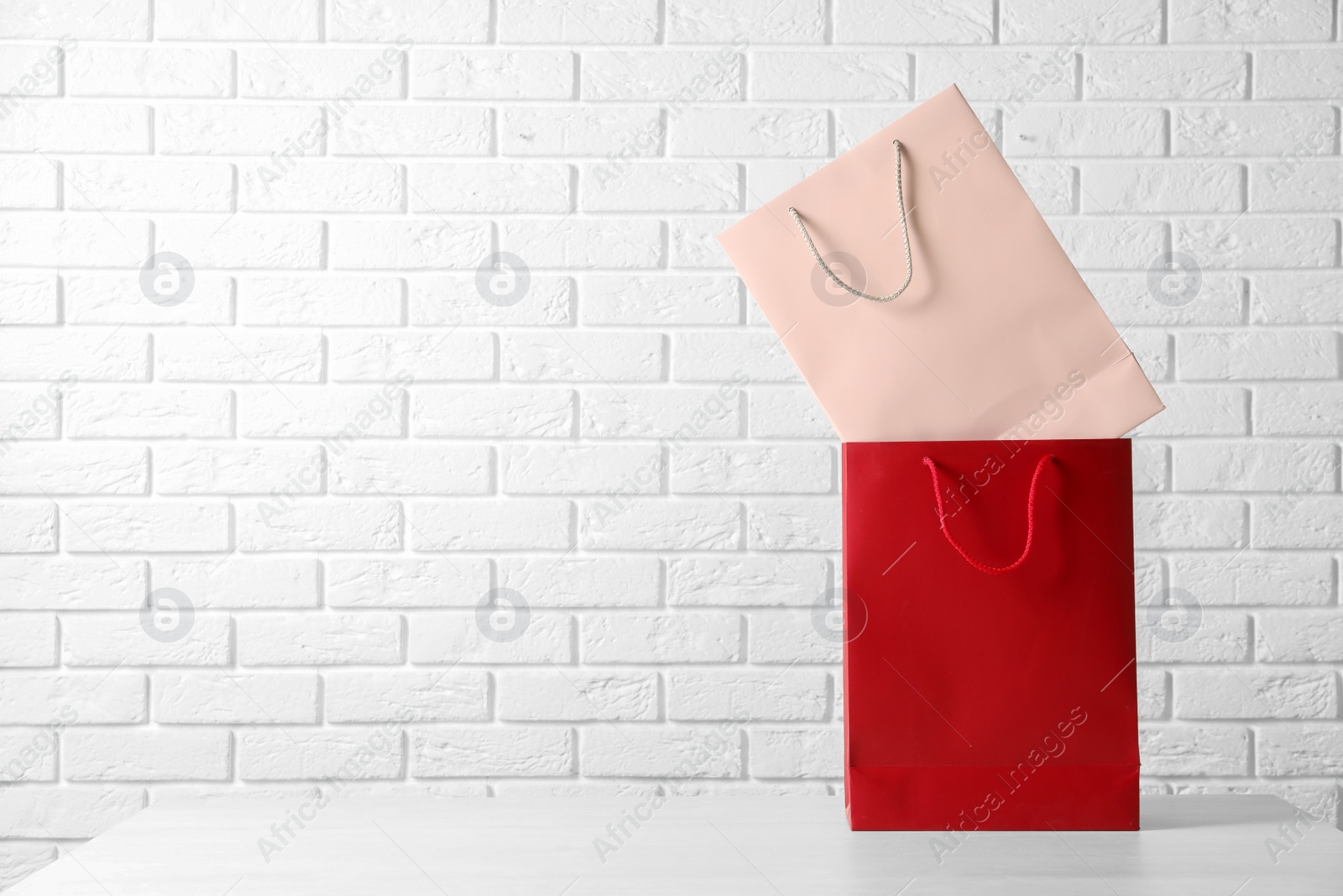 Photo of Colorful paper shopping bags on table against brick wall. Space for text