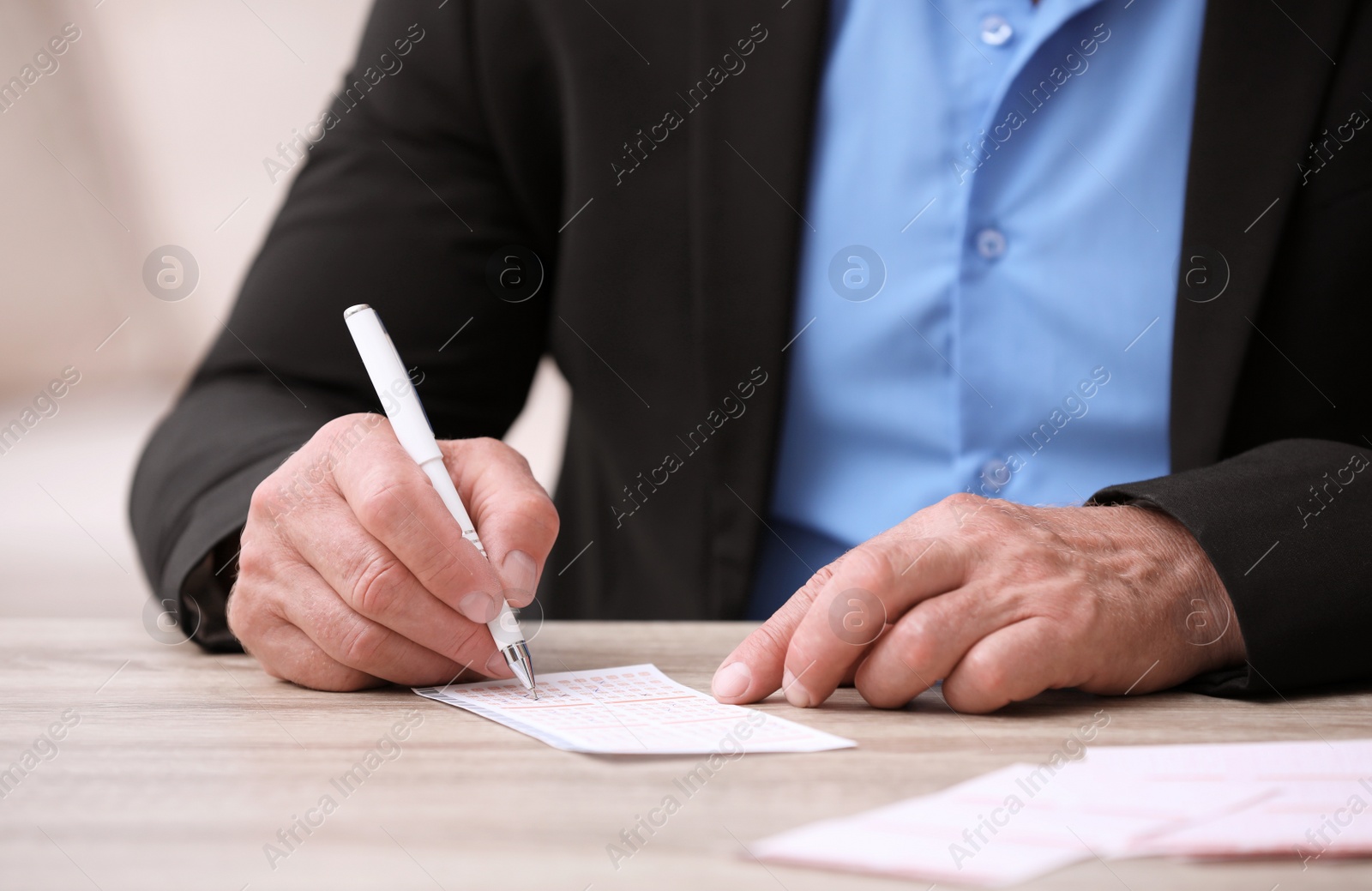 Photo of Senior man filling out lottery ticket at table, closeup