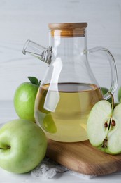 Photo of Jug of tasty juice and fresh ripe green apples on white wooden table, closeup