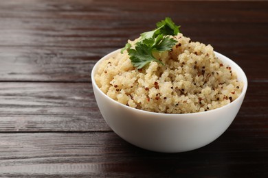 Photo of Tasty quinoa porridge with parsley in bowl on wooden table, closeup. Space for text