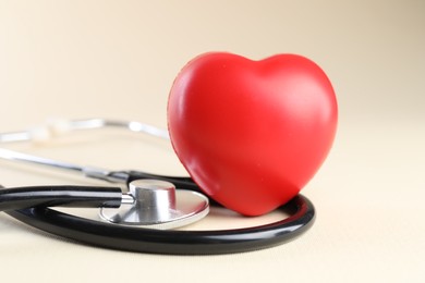 Photo of Stethoscope and red heart on beige background, closeup