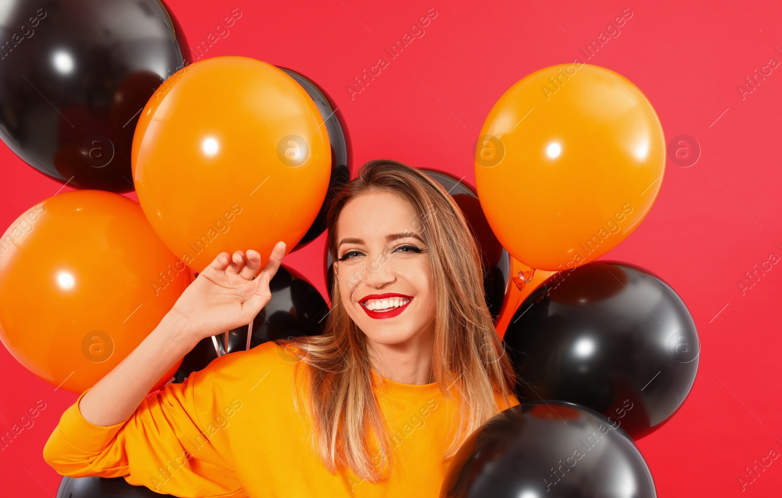 Photo of Beautiful woman with balloons on red background. Halloween party