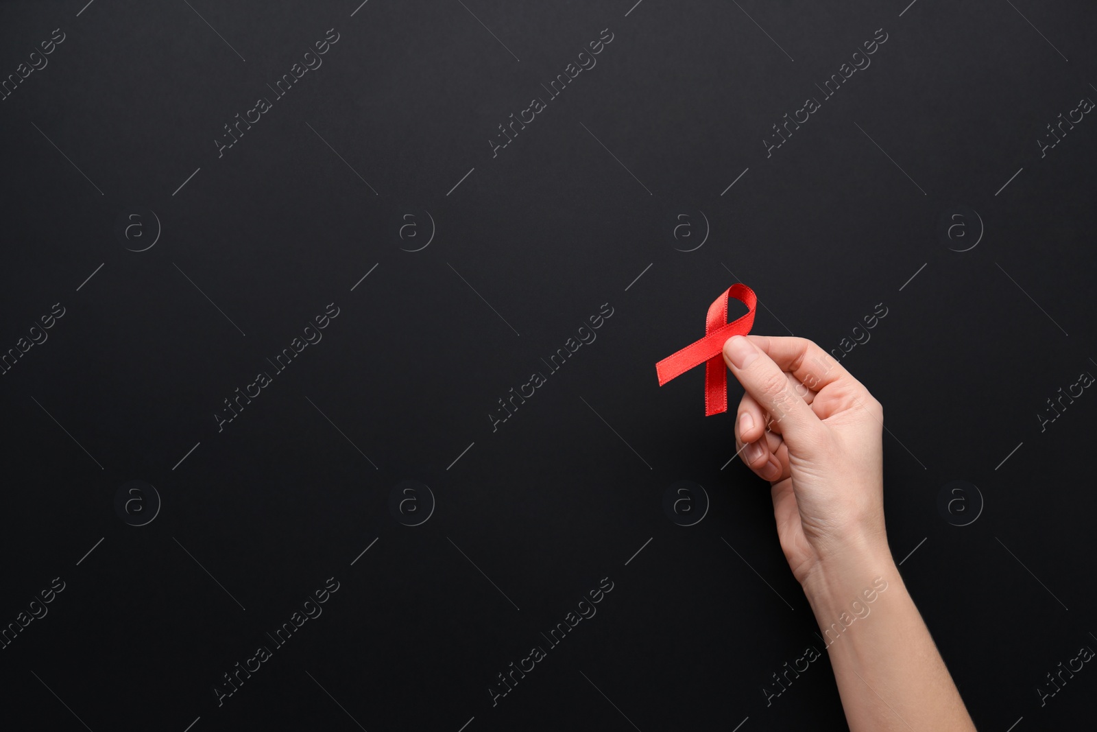 Photo of Woman holding red awareness ribbon on black background, top view with space for text. World AIDS disease day