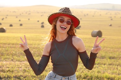Photo of Beautiful happy hippie woman in hat showing peace signs in field