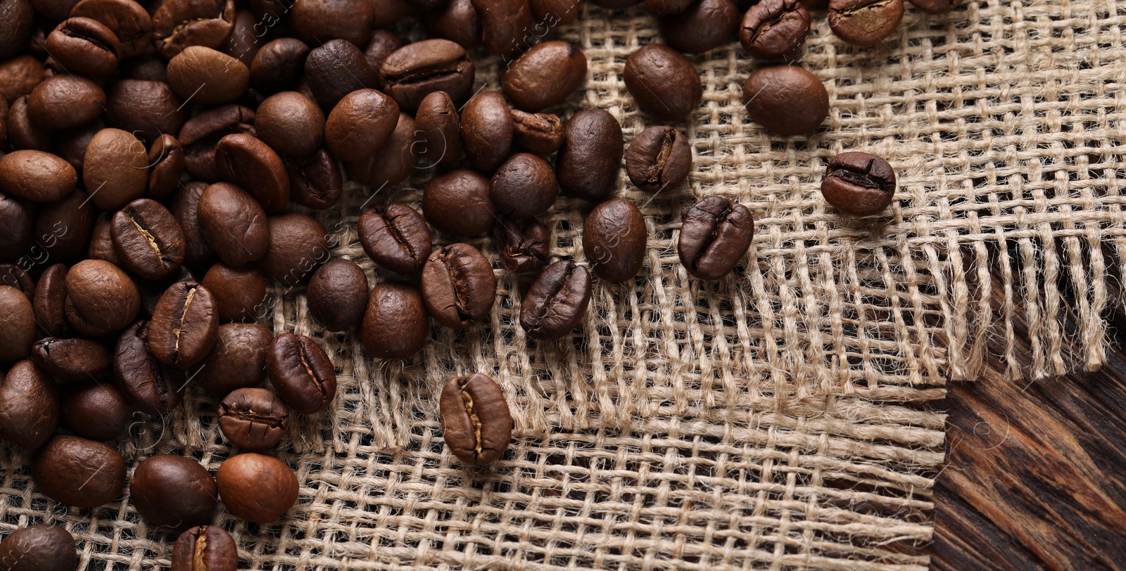 Photo of Many coffee beans and burlap fabric on wooden table, top view. Space for text