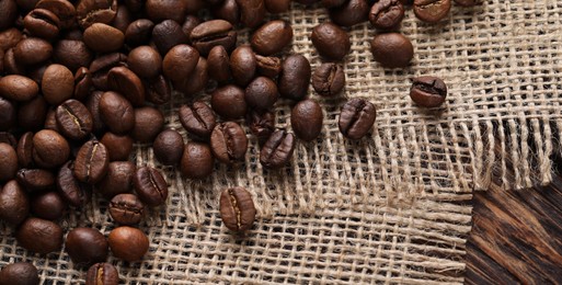 Photo of Many coffee beans and burlap fabric on wooden table, top view. Space for text