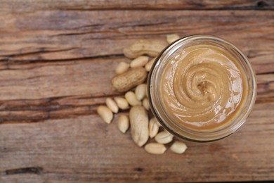 Photo of Tasty peanut nut paste in jar on wooden table, top view. Space for text