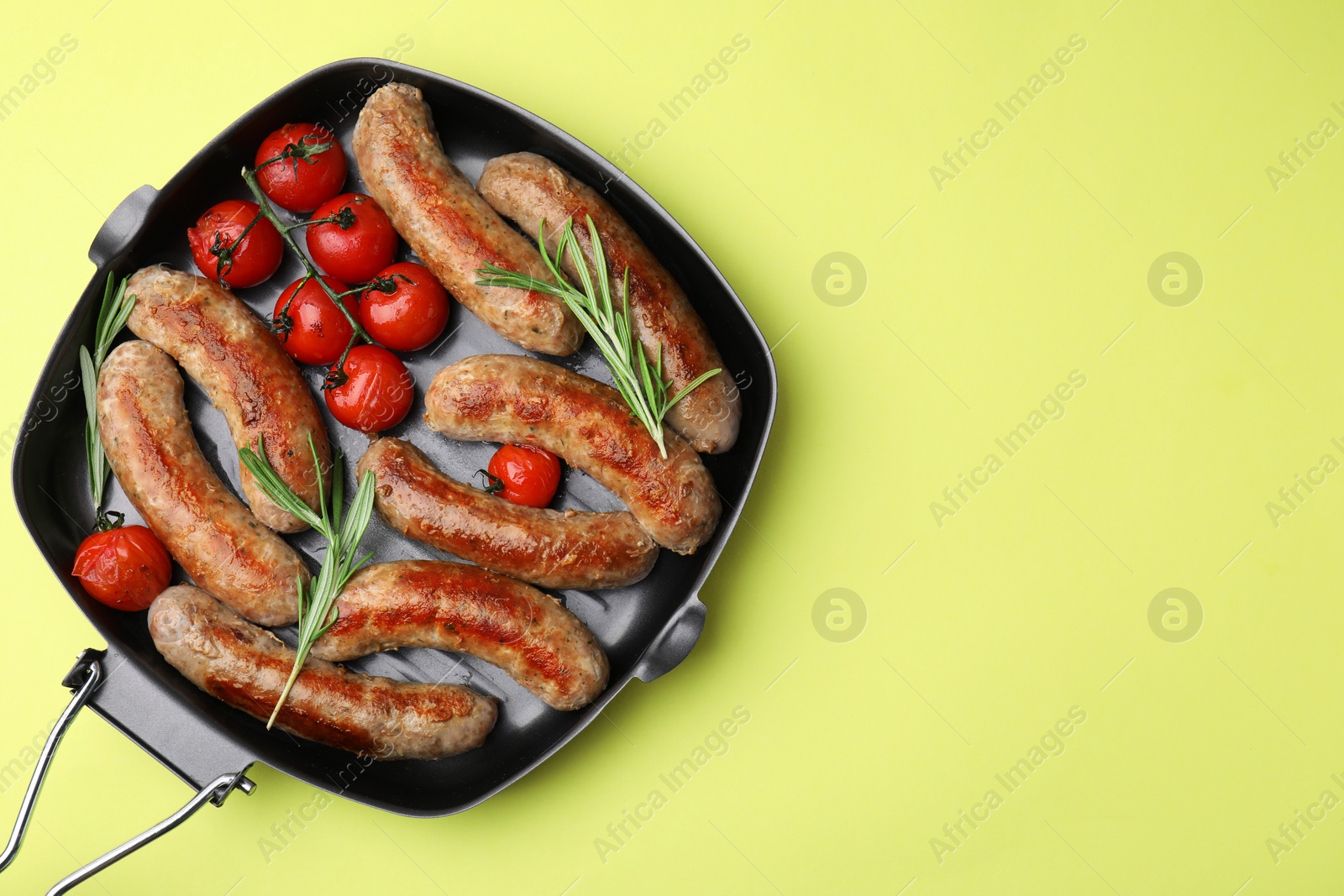 Photo of Grill pan with tasty homemade sausages, rosemary and tomatoes on yellow table, top view. Space for text