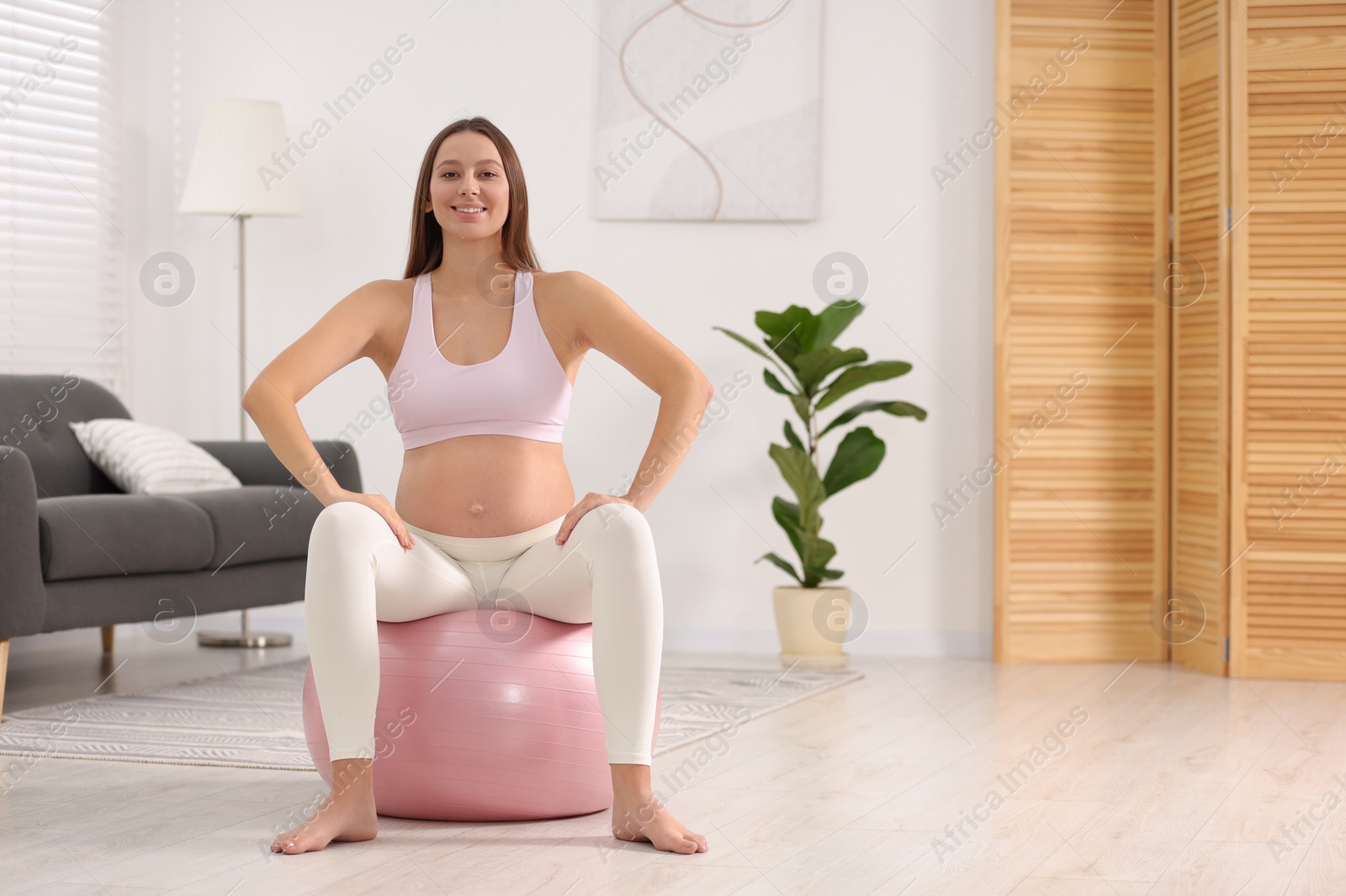 Photo of Pregnant woman doing exercises on fitness ball in room, space for text. Home yoga