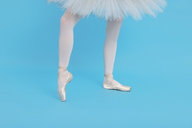 Young ballerina in pointe shoes practicing dance moves on light blue background, closeup