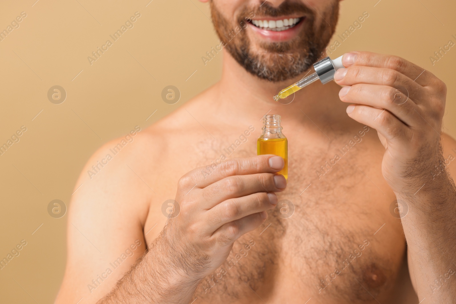 Photo of Smiling man with cosmetic serum on beige background, selective focus