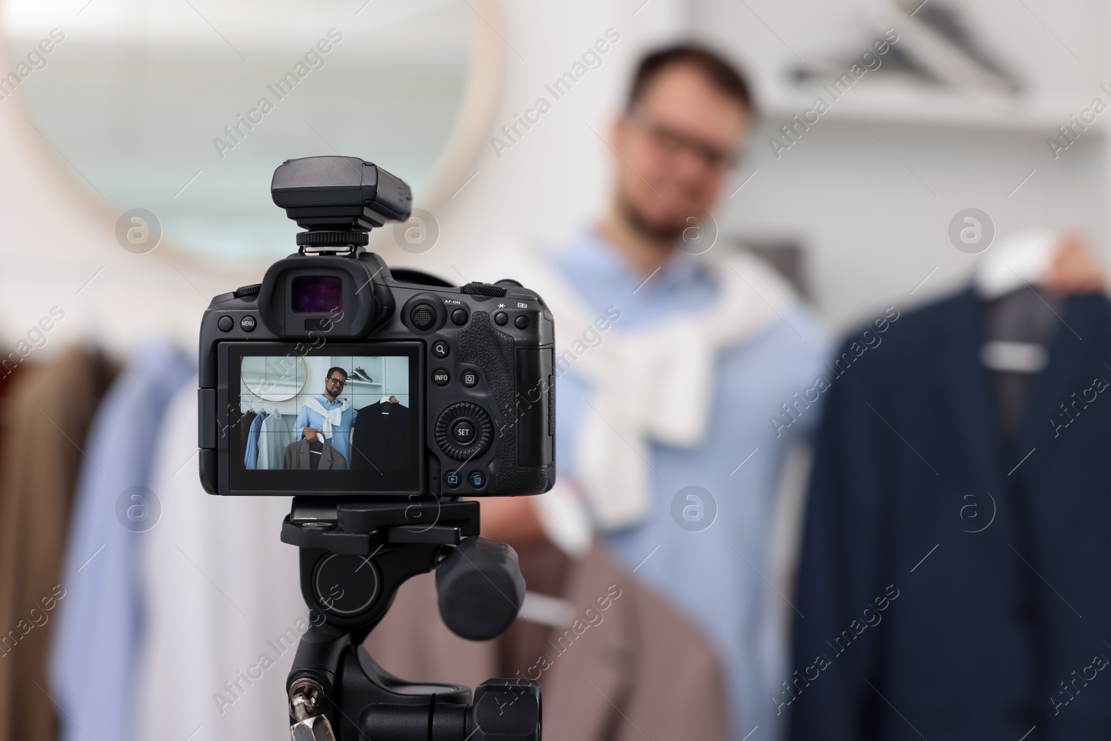 Photo of Fashion blogger showing clothes while recording video at home, focus on camera