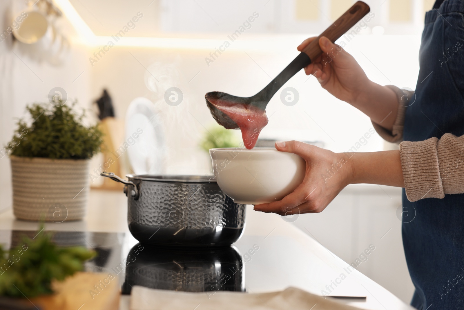 Photo of Woman pouring tasty soup into bowl at countertop in kitchen, closeup