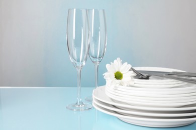 Set of clean dishes, glasses and cutlery on light blue table, space for text