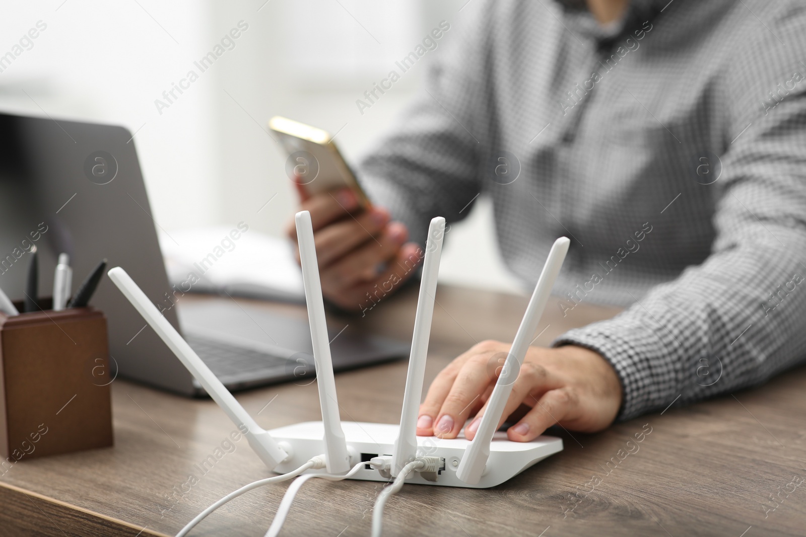 Photo of Man with smartphone and laptop connecting to internet via Wi-Fi router at wooden table, closeup