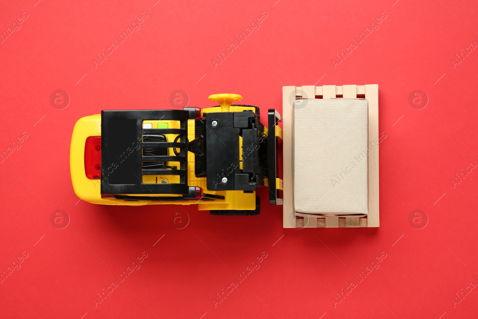 Photo of Toy forklift with wooden pallet and box on red background, top view