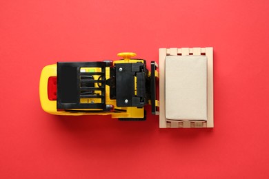Toy forklift with wooden pallet and box on red background, top view