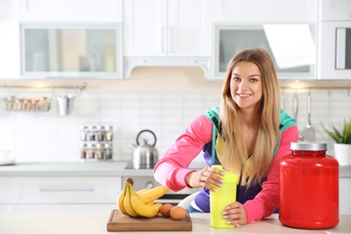 Photo of Young woman preparing protein shake at table in kitchen. Space for text