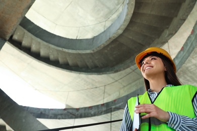 Professional engineer in safety equipment with clipboard at construction site. Space for text