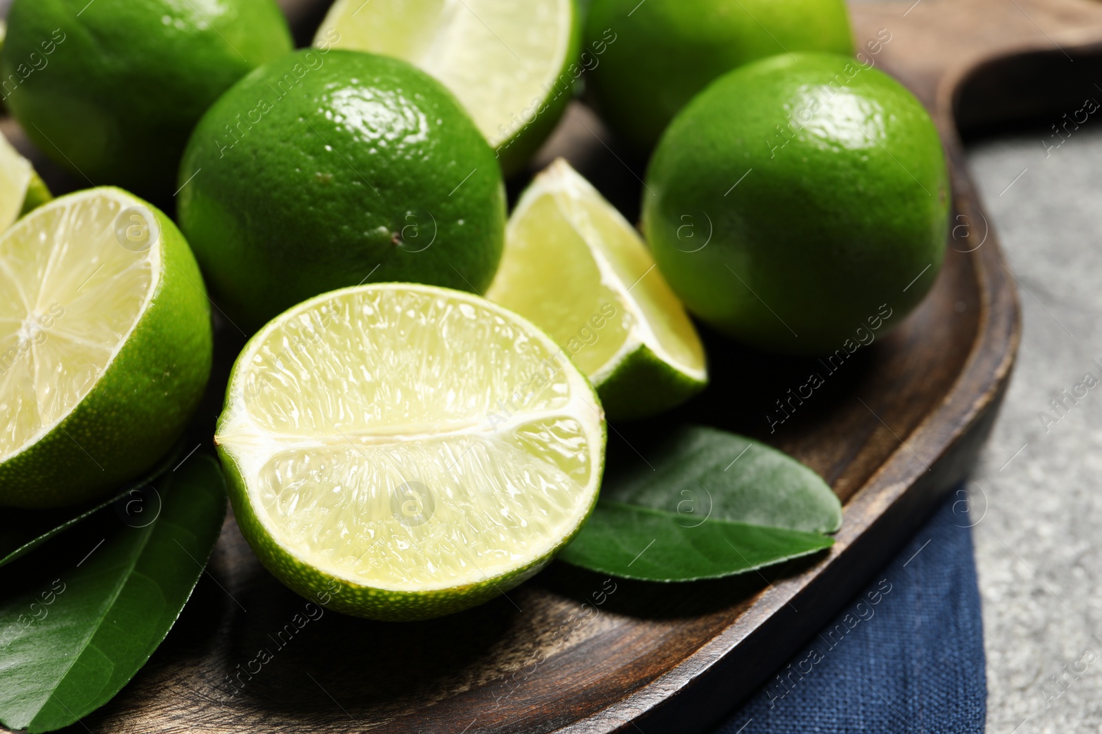 Photo of Fresh ripe limes and leaves on grey table, closeup