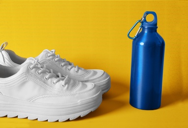 Photo of Stylish sneakers and sport bottle with water on color background. Healthy lifestyle