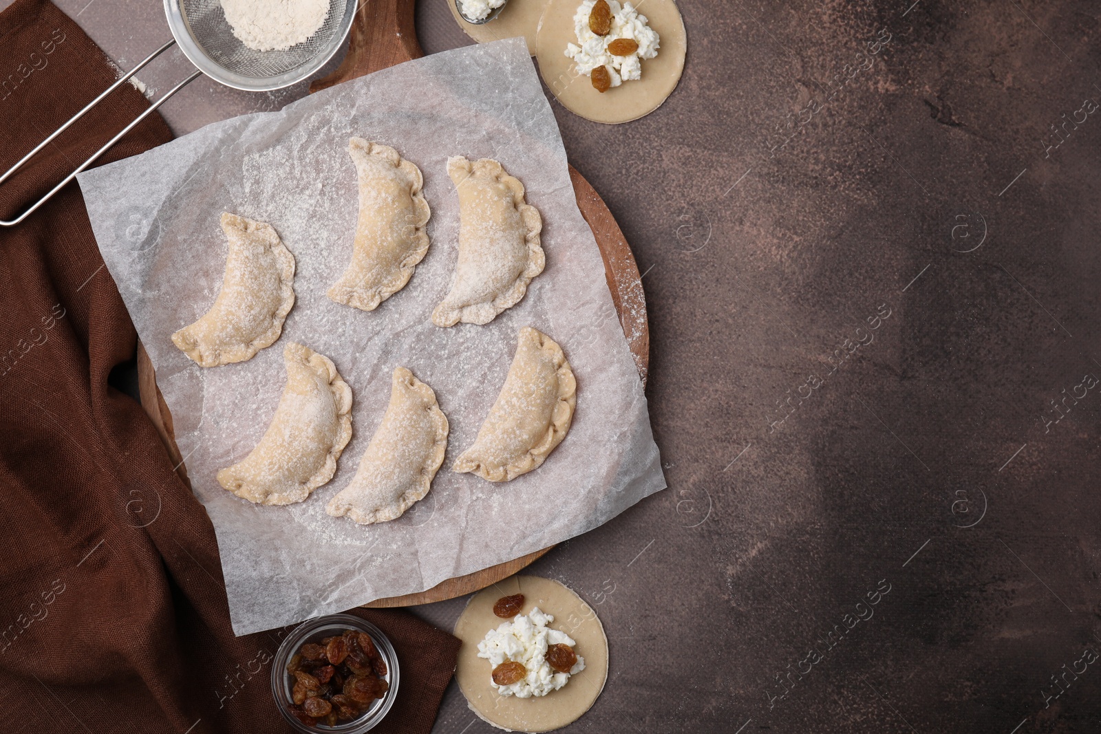 Photo of Process of making dumplings (varenyky) with cottage cheese. Raw dough and ingredients on brown table, flat lay. Space for text