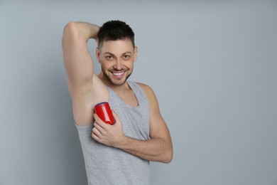 Photo of Handsome man applying deodorant on grey background. Space for text