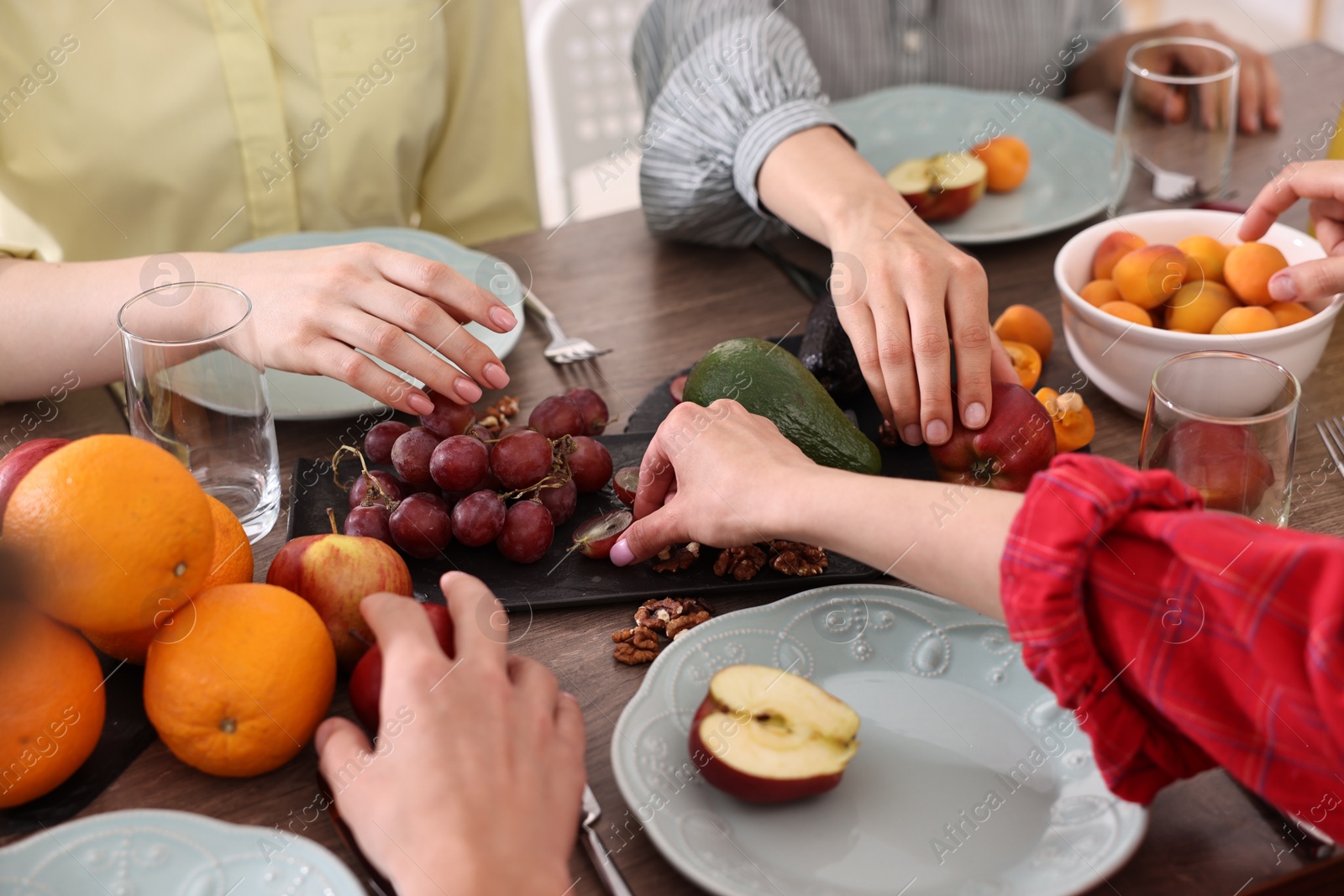 Photo of Vegetarian food. Friends eating fresh fruits at wooden table indoors, closeup