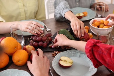 Vegetarian food. Friends eating fresh fruits at wooden table indoors, closeup