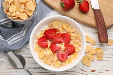 Photo of Bowl of tasty crispy corn flakes with milk and strawberries on white wooden table, flat lay