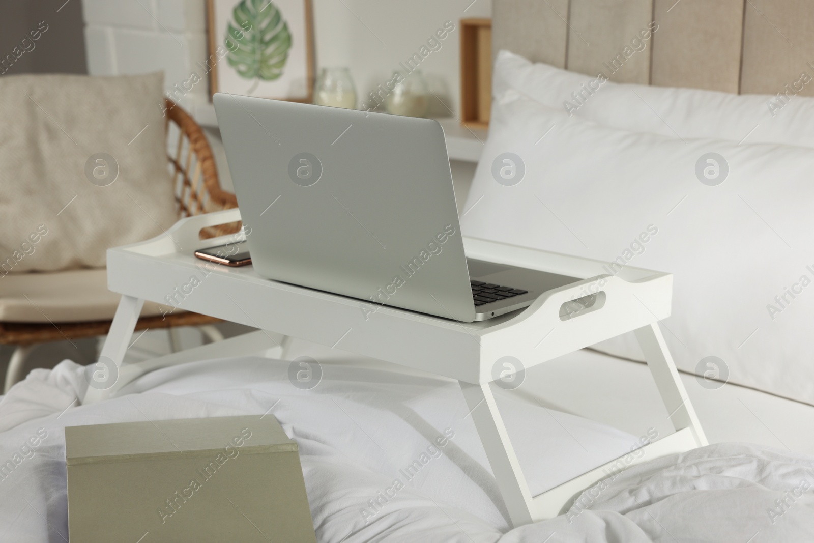 Photo of White tray with modern laptop and smartphone on bed indoors