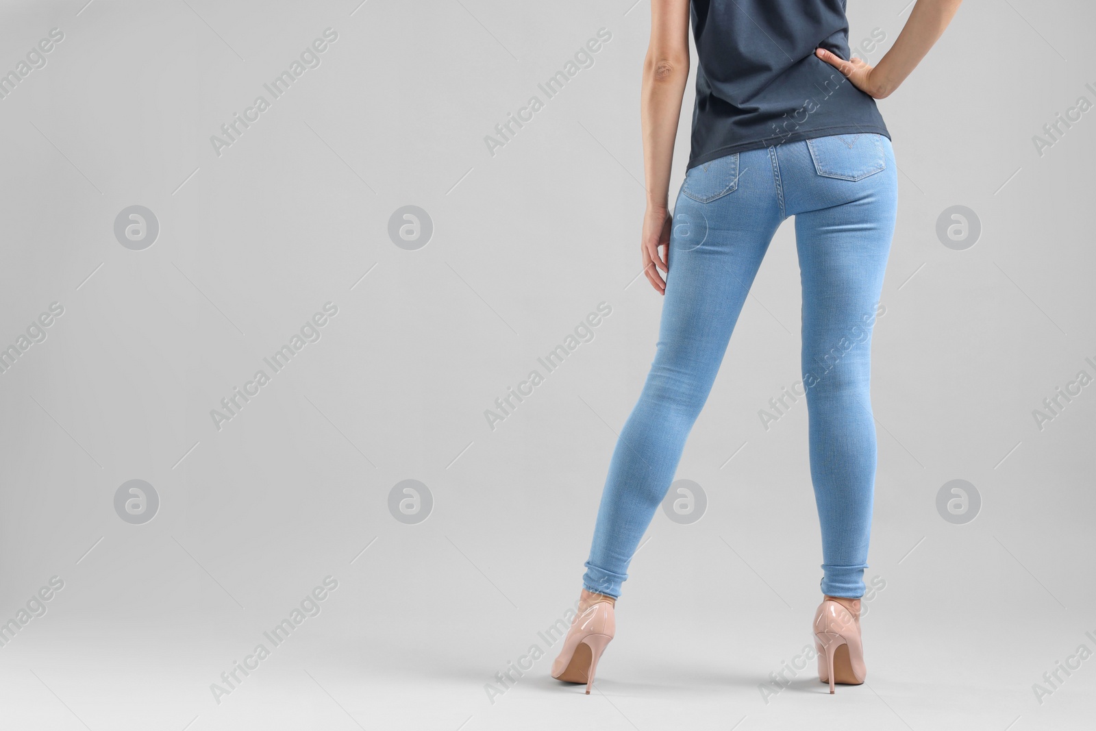 Photo of Woman wearing stylish jeans and high heels shoes on light gray background, closeup. Space for text