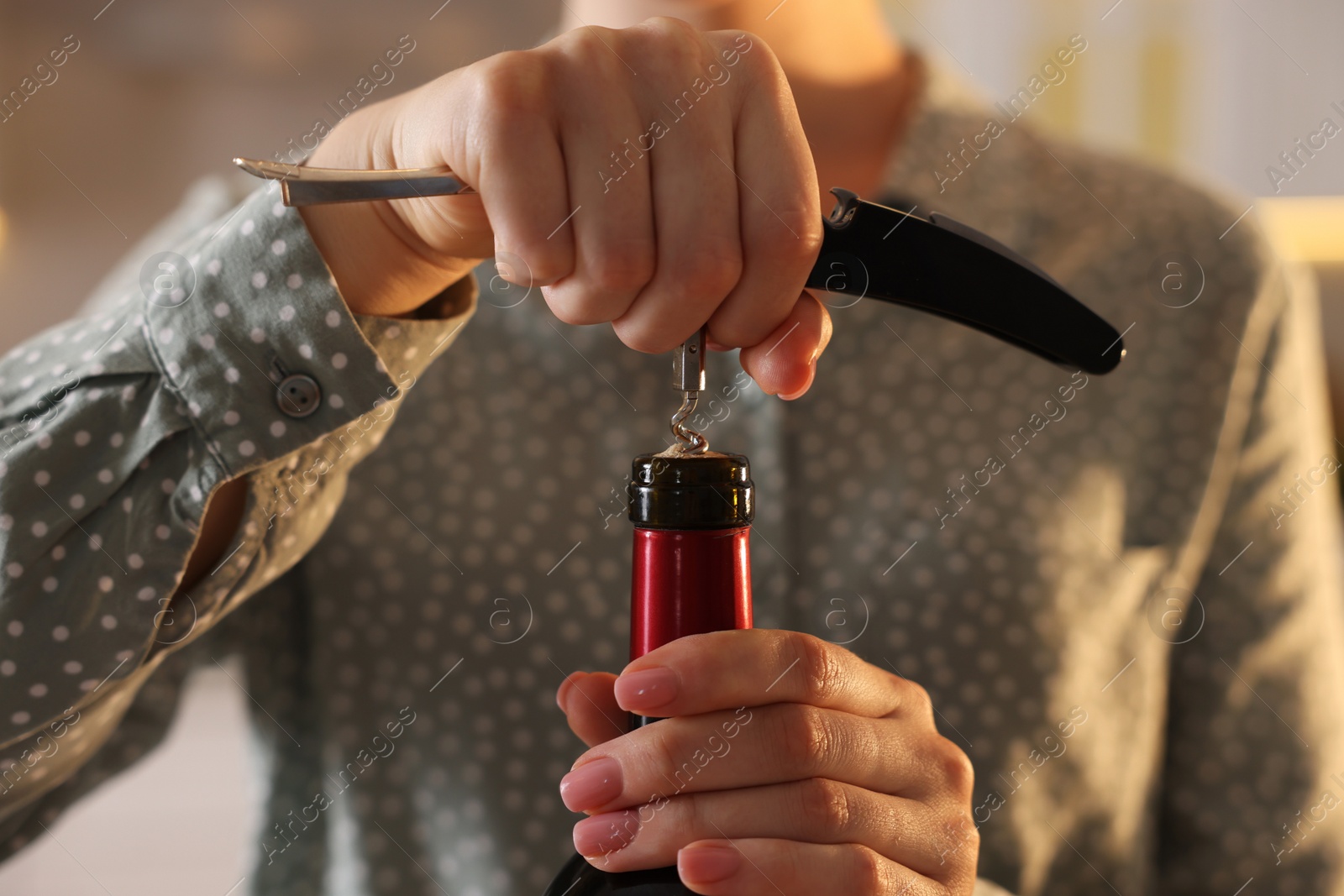 Photo of Woman opening wine bottle with corkscrew indoors, closeup